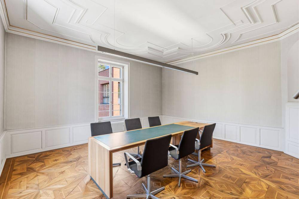 Konferenzraum mit elegantem Parkettboden, dekorativer Decke und einem Fenster mit Blick auf die Stadt.