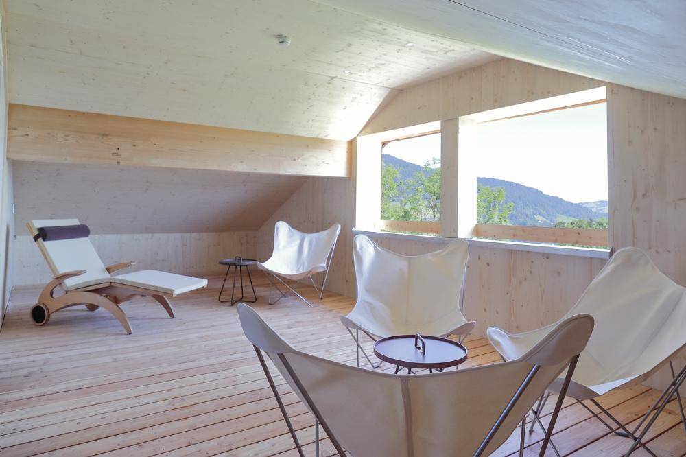 Heller Entspannungsbereich im Dachgeschoss mit Holzverkleidung, bequemen Sesseln und Bergblick.