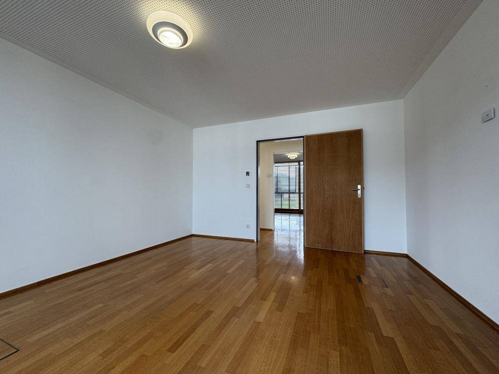 Heller Raum mit Holzboden und einer Holztür, die zu einem weiteren Bereich führt.