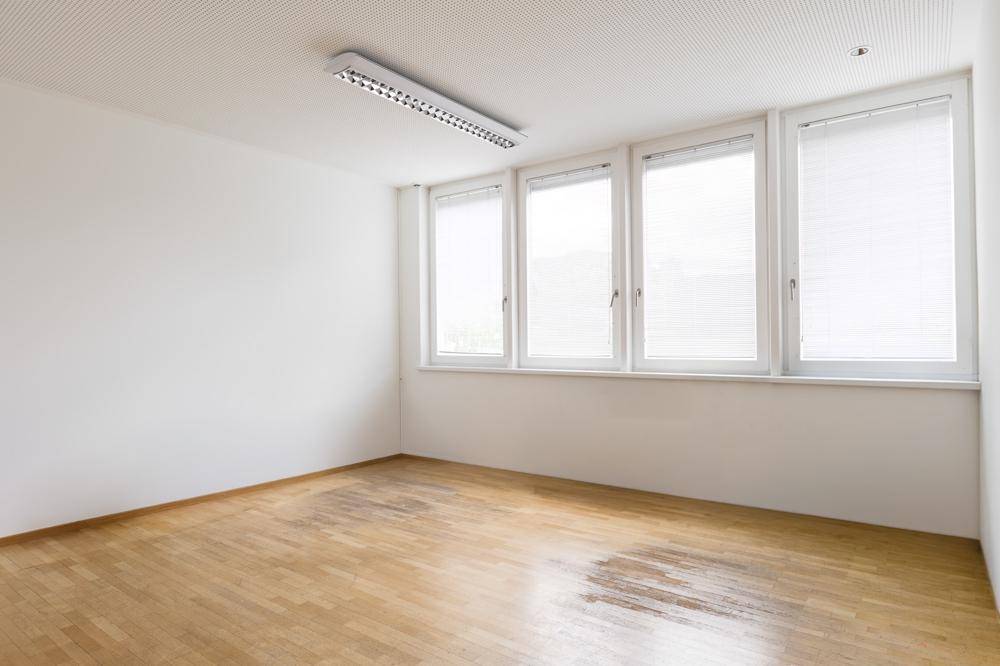 Leerer Büroraum mit Parkettboden, großen Fenstern und einer Deckenleuchte.