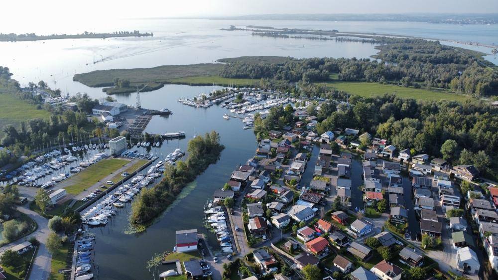 Panoramische Luftaufnahme einer Küstenlandschaft mit einem großen See, Yachthäfen und einer Siedlung am Ufer.