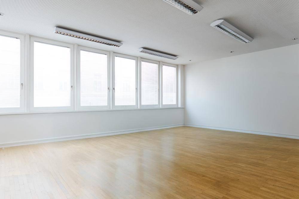 Geräumiger Büroraum mit Parkettboden, vielen Fenstern und mehreren Deckenleuchten.