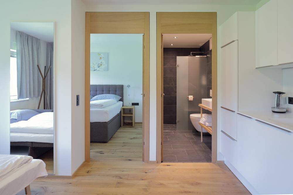 Blick durch offene Türen auf ein Schlafzimmer, ein Badezimmer und eine Küchenzeile.
