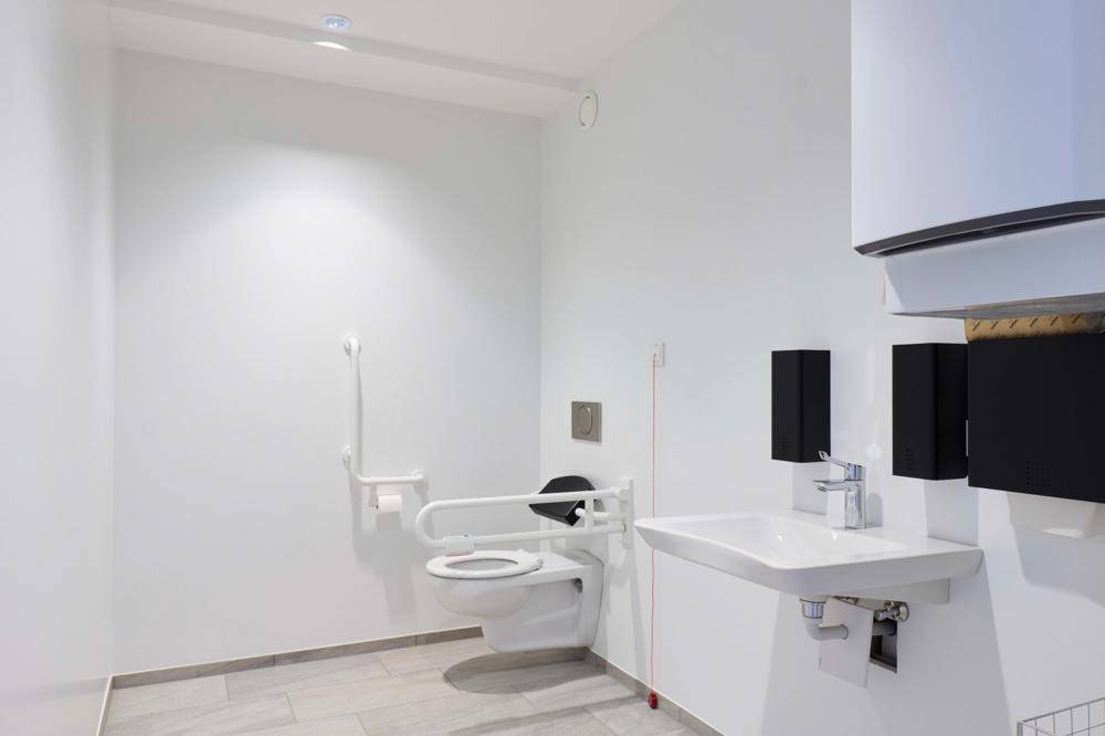 Barrierefreie Toilette mit Haltegriffen, wandhängendem WC und modernem Waschbecken.