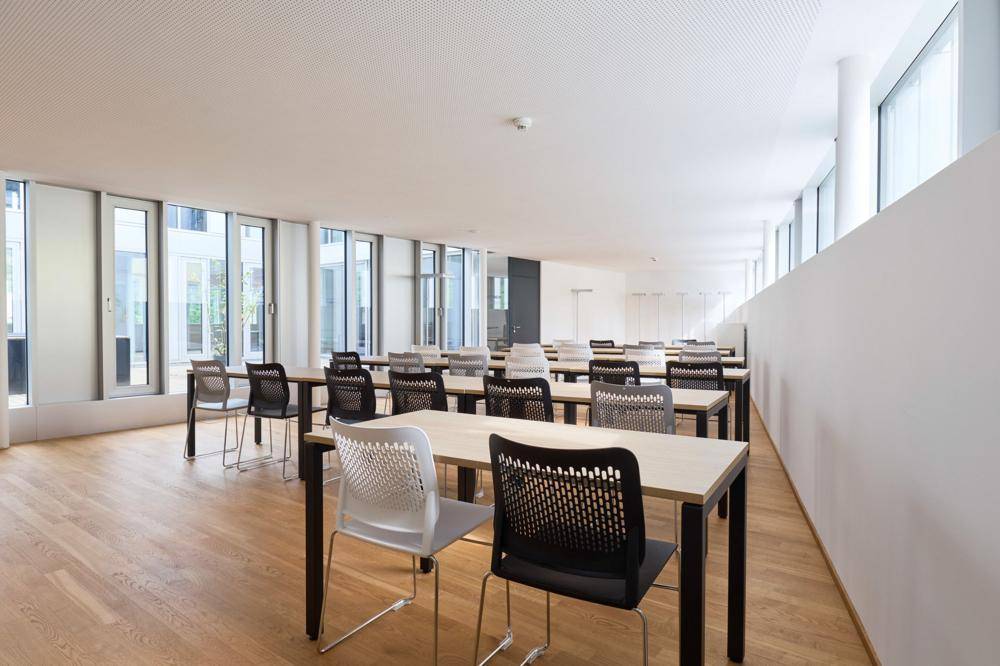 Großer Konferenz- oder Schulungsraum mit Holzboden, vielen Tischen und Stühlen, hell und modern.