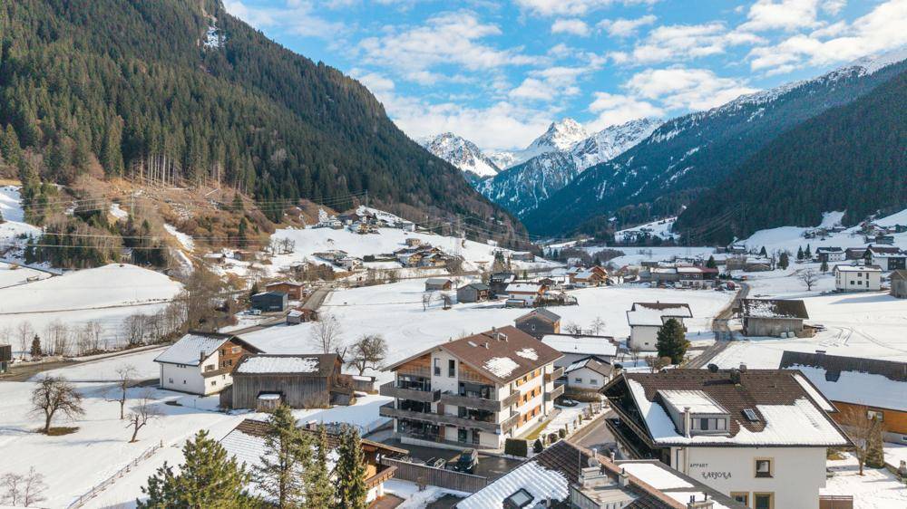 Panoramablick auf ein verschneites Dorf in einem malerischen Alpental mit umliegenden Bergen.