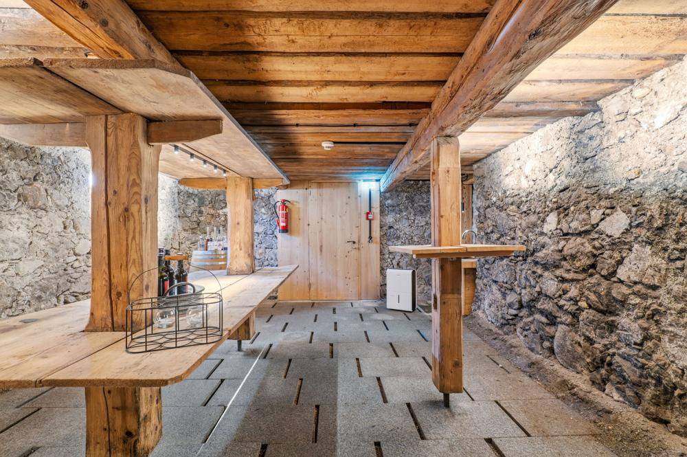 Geräumiger Kellerraum mit Holzbalken, Steinwänden und Holztischen.
