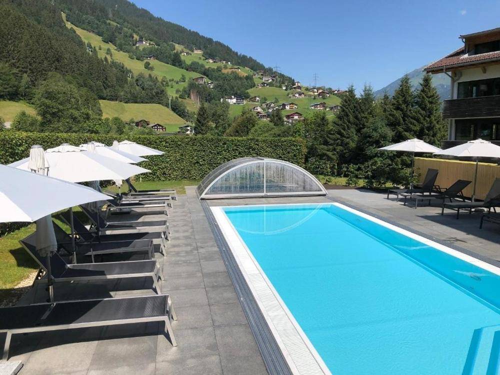 Großer Außenpool mit Liegestühlen und Sonnenschirmen vor einer malerischen Bergkulisse.