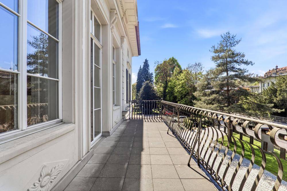 Langer Balkon mit schmiedeeisernem Geländer und Fliesenboden, bietet einen schönen Blick auf den grünen Park.