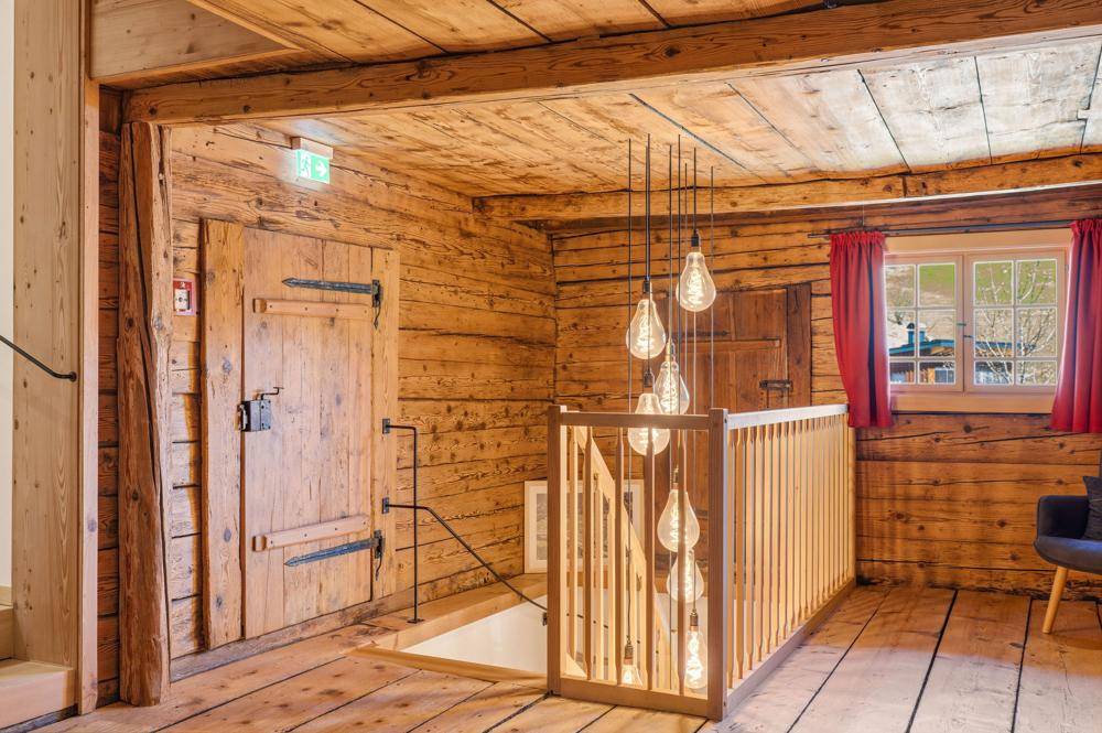 Rustikaler Flur mit Holzwänden, Holzboden und einer Treppe mit moderner Beleuchtung.