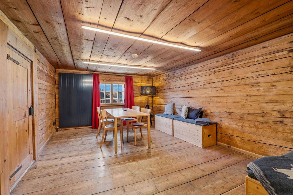 Wohnzimmer mit Holzwänden, Holzboden, Esstisch und einer gemütlichen Sitzbank.