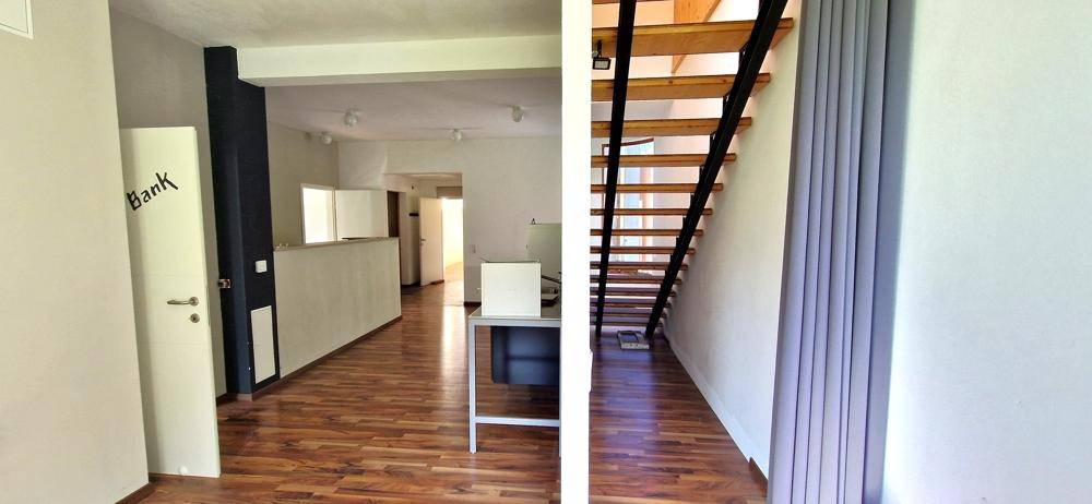 Empfangsbereich mit Holzfußboden, moderner Treppe und Zugang zu weiteren Räumen, gut beleuchtet.
