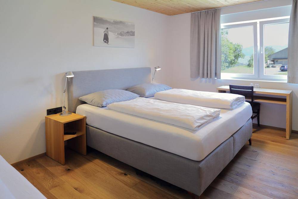 Komfortables Schlafzimmer mit Doppelbett, Holzboden und Schreibtisch am Fenster mit Ausblick.