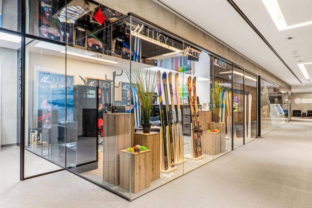 Heller Ladenbereich mit Skiausrüstung und Holzdisplays, umgeben von Glaswänden in einem modernen Gebäude.