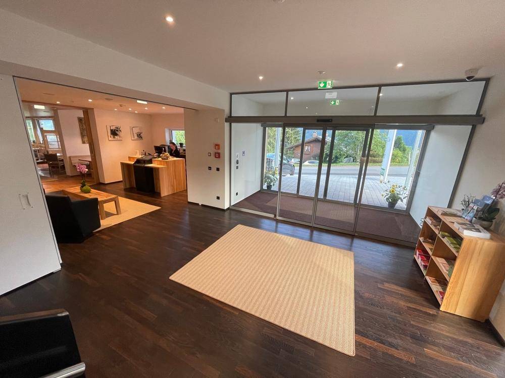 Heller Empfangsbereich mit Holzboden, Teppich und Blick durch große Glastüren nach draußen.