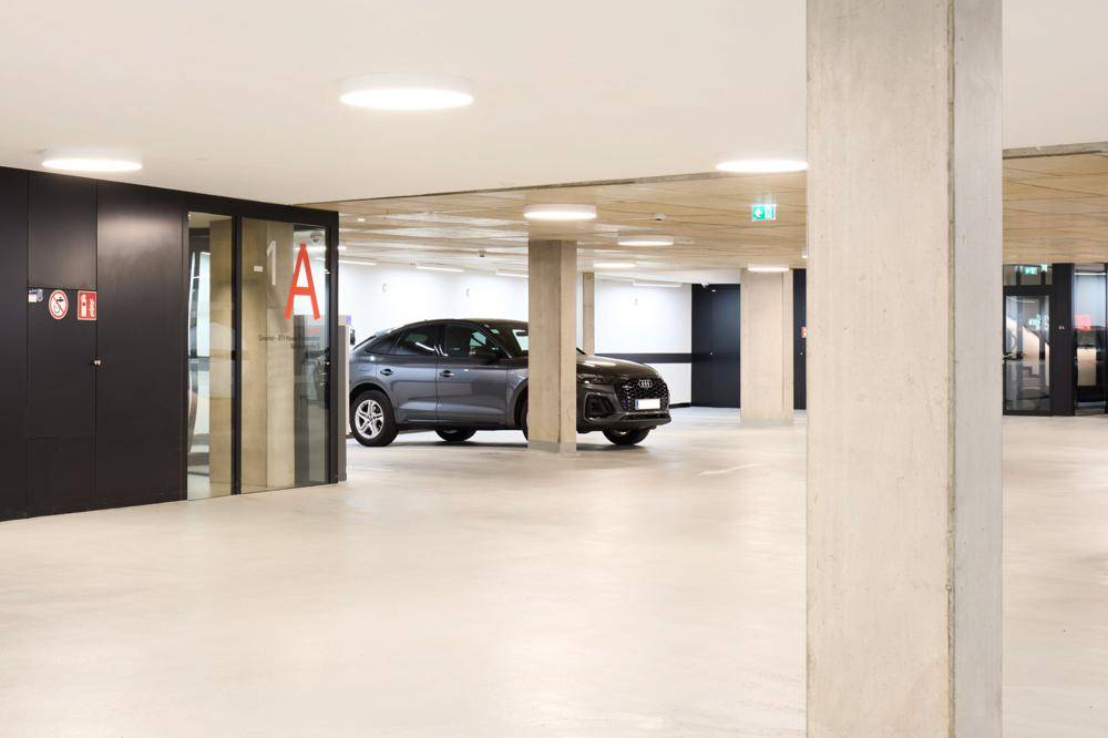 Moderne Tiefgarage mit ausreichend Stellplätzen, Betonpfeilern und heller Beleuchtung, bietet sicheres Parken.