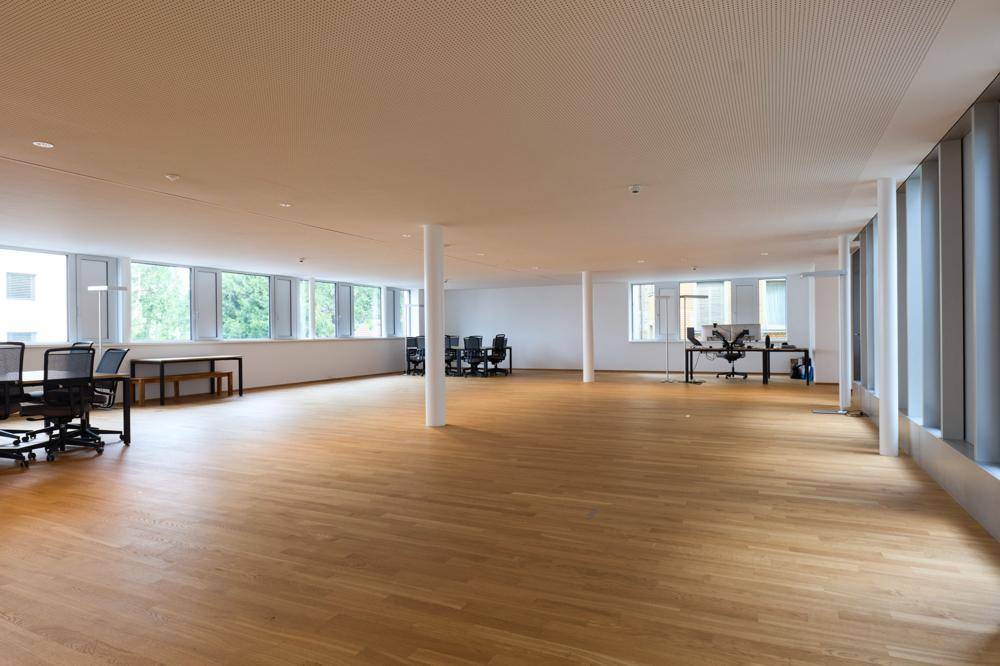 Großzügiger, offener Bürobereich mit Holzboden, vielen Fenstern und modernen Arbeitsplätzen.