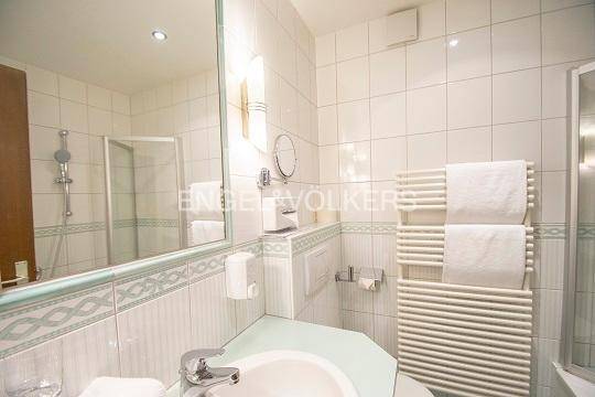 Helles Badezimmer mit weißen Fliesen, Dusche, Waschbecken und Handtuchheizkörper.