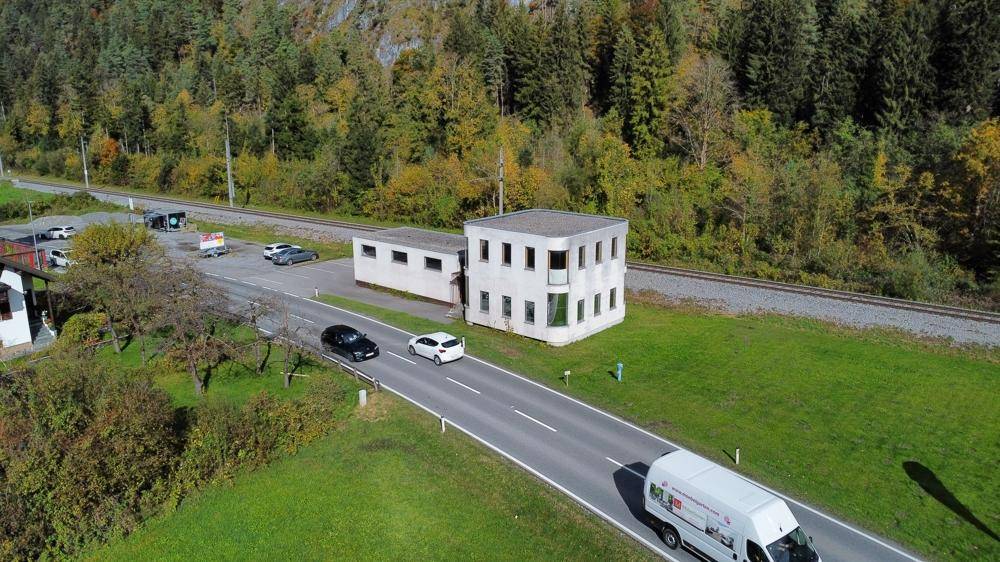 Gebäudeansicht aus der Vogelperspektive mit Straße und Bahngleisen in ländlicher Umgebung.