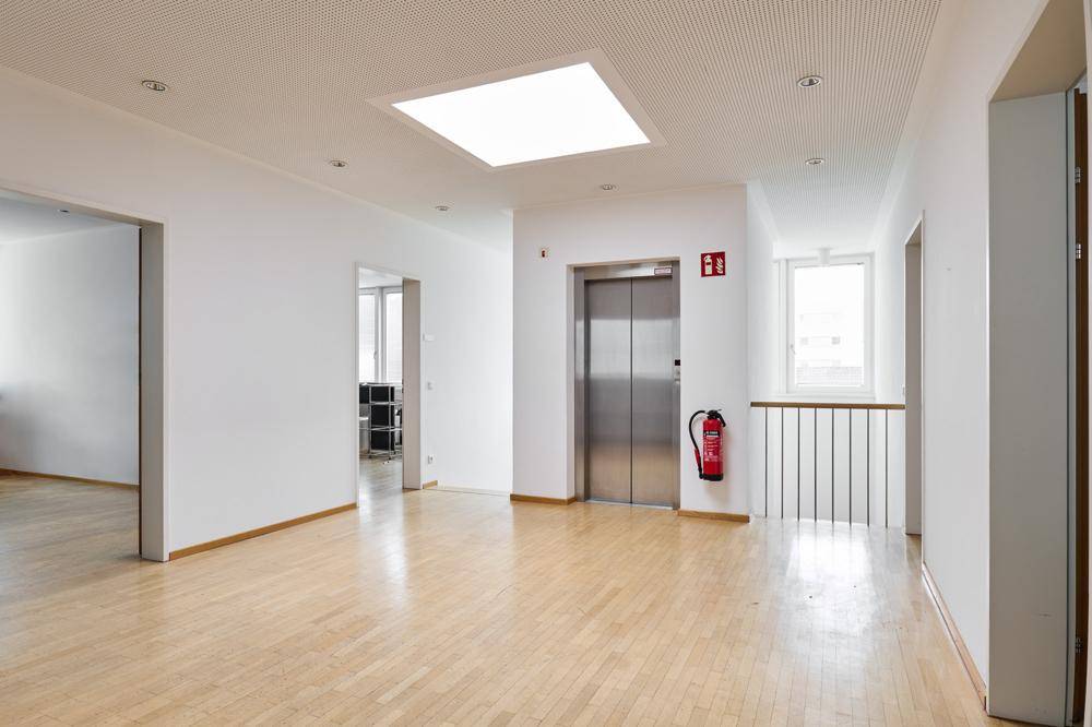 Heller Flur mit Aufzug, Parkettboden und einem großen Oberlicht, das den Raum erhellt.