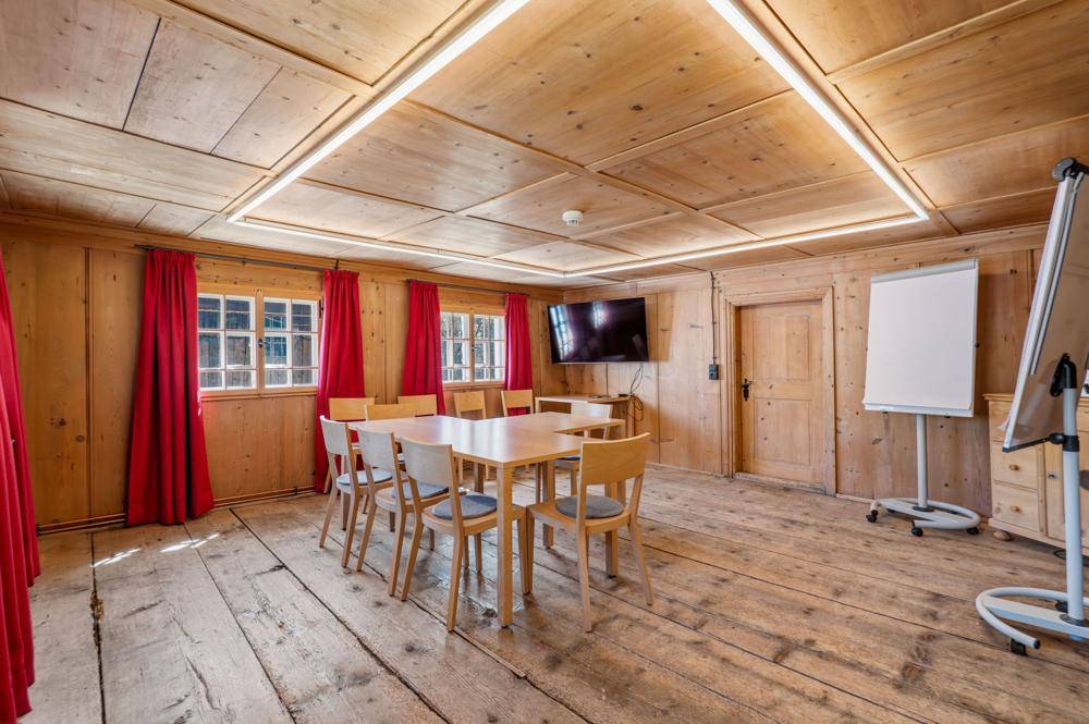 Konferenzraum mit Holzwänden, Holzboden, großem Tisch und einem Wandfernseher.