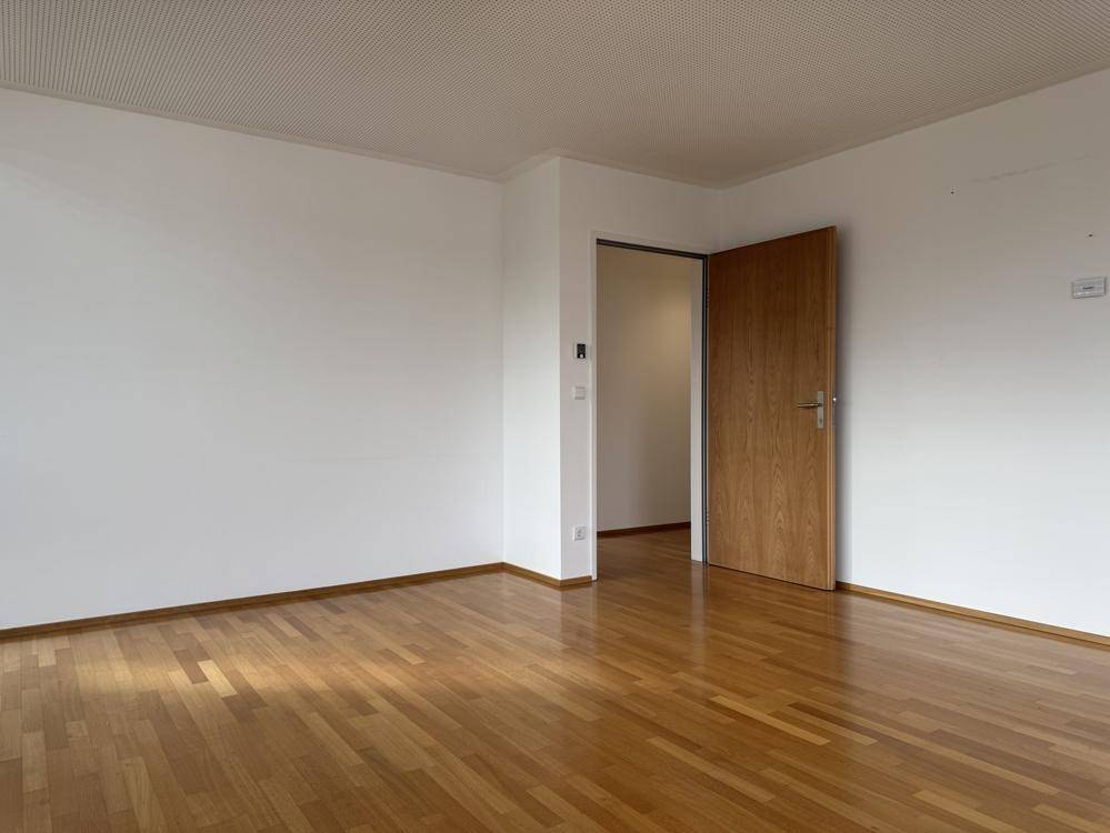 Leerer Raum mit Holzboden und einer Holztür, die zu einem weiteren Bereich führt.