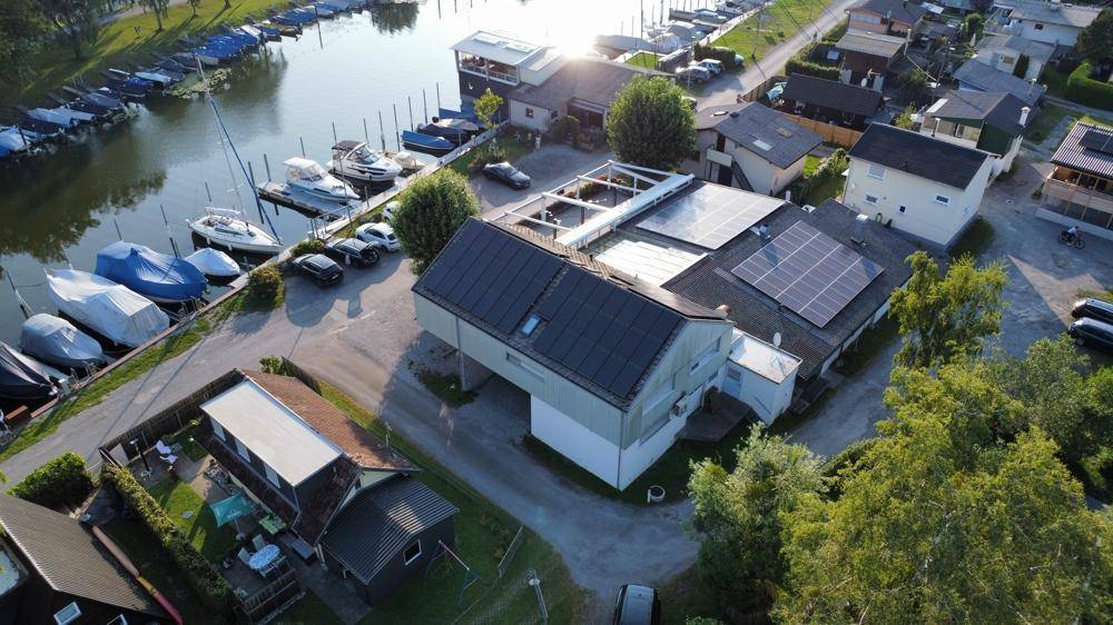 Luftaufnahme des Anwesens mit Solaranlagen auf den Dächern, umgeben von Bäumen und einem belebten Yachthafen.