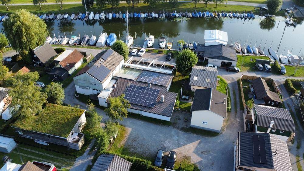 Übersichtliche Luftaufnahme des gesamten Anwesens mit mehreren Gebäuden, Solaranlagen und angrenzendem Yachthafen.