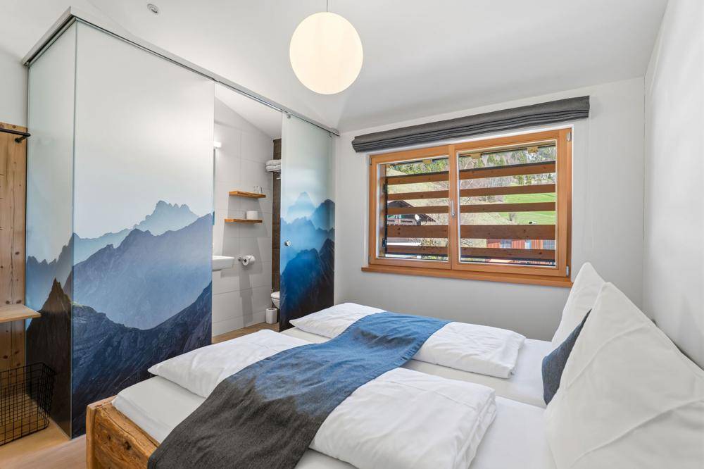 Helles Schlafzimmer mit zwei Einzelbetten, Schiebetüren zum Bad und Fenster mit Bergblick.