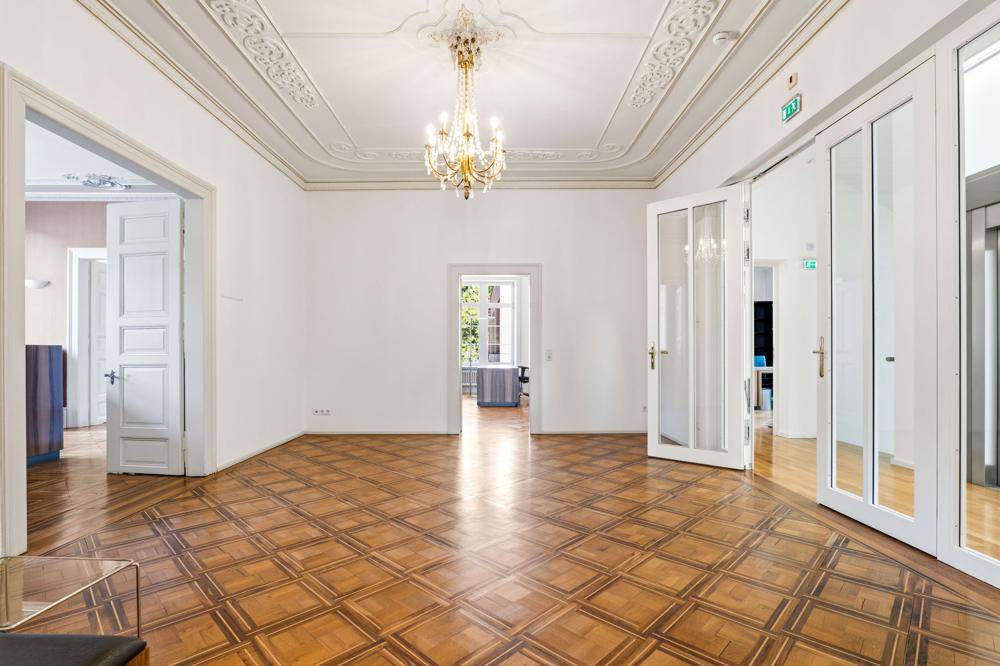 Geräumiger Büroraum mit kunstvoller Stuckdecke, klassischem Parkettboden und hohen Flügeltüren.