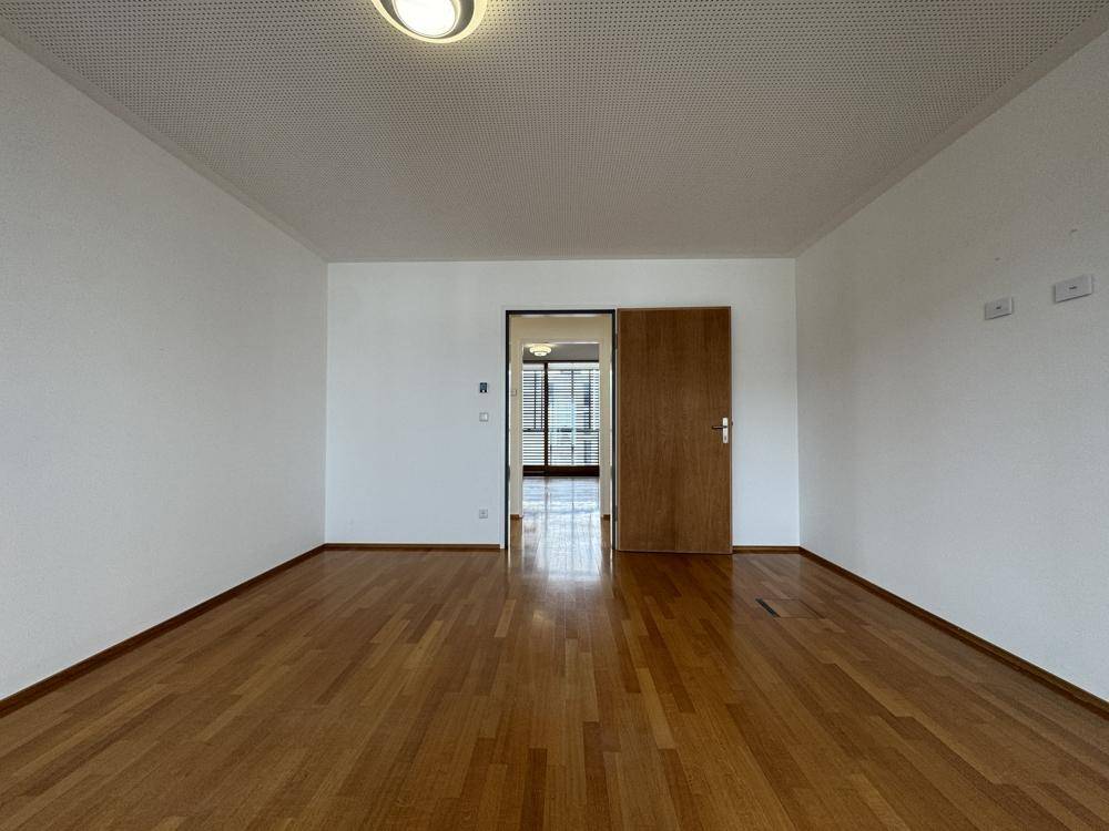 Heller Raum mit Holzboden und einer Holztür, die zu einem weiteren Bereich führt.