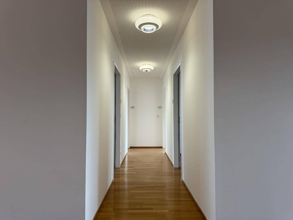 Heller Flur mit Holzparkettboden und modernen Deckenleuchten, der zu weiteren Räumen führt.