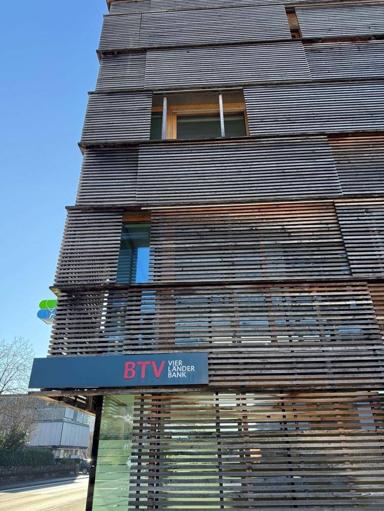 Nahaufnahme der modernen Holzlamellenfassade eines Geschäftsgebäudes mit Bankfiliale im Erdgeschoss.