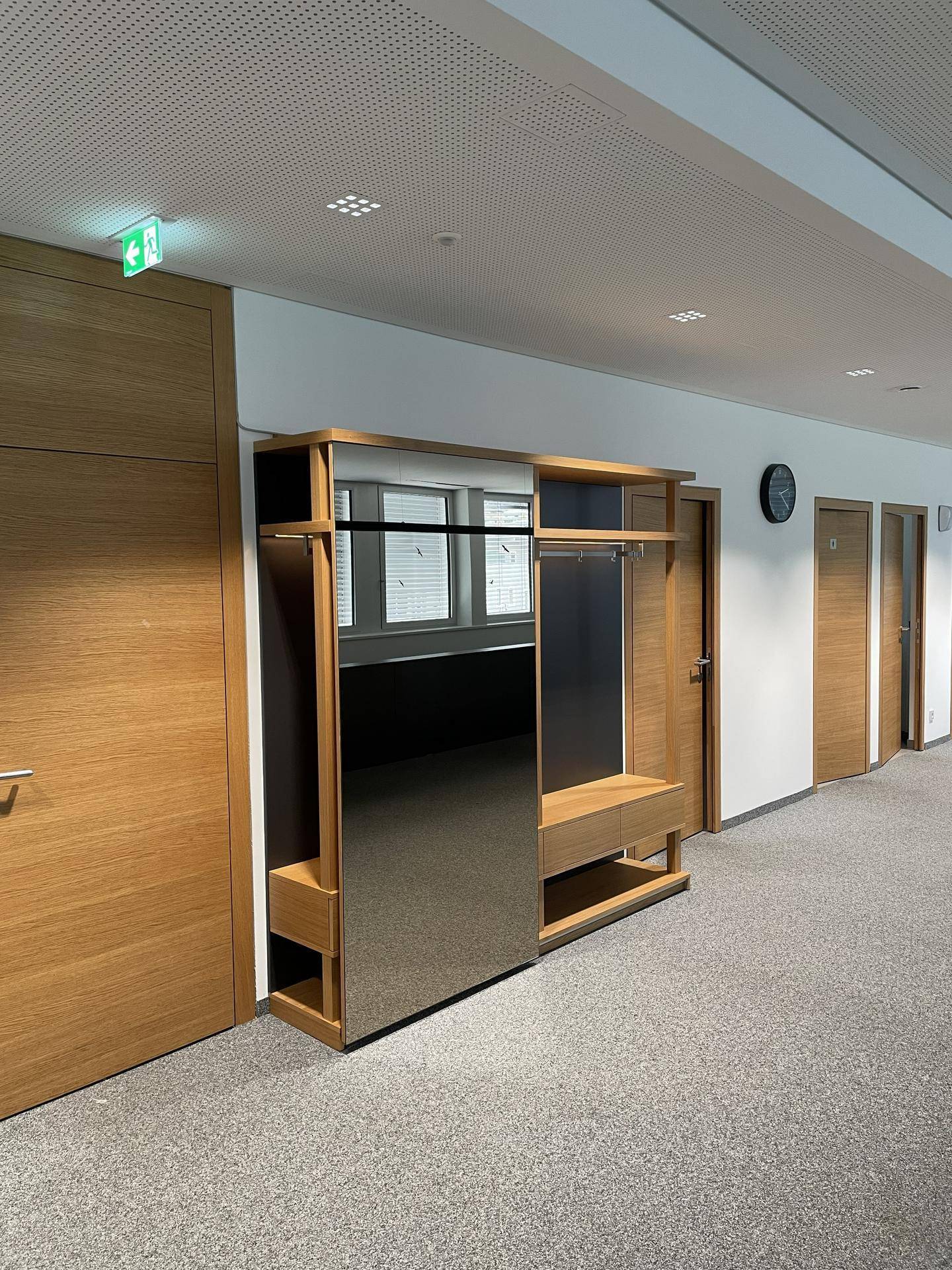 Moderner Flur mit grauem Teppichboden und einem stilvollen Garderobenmöbel mit großer Spiegelfläche.