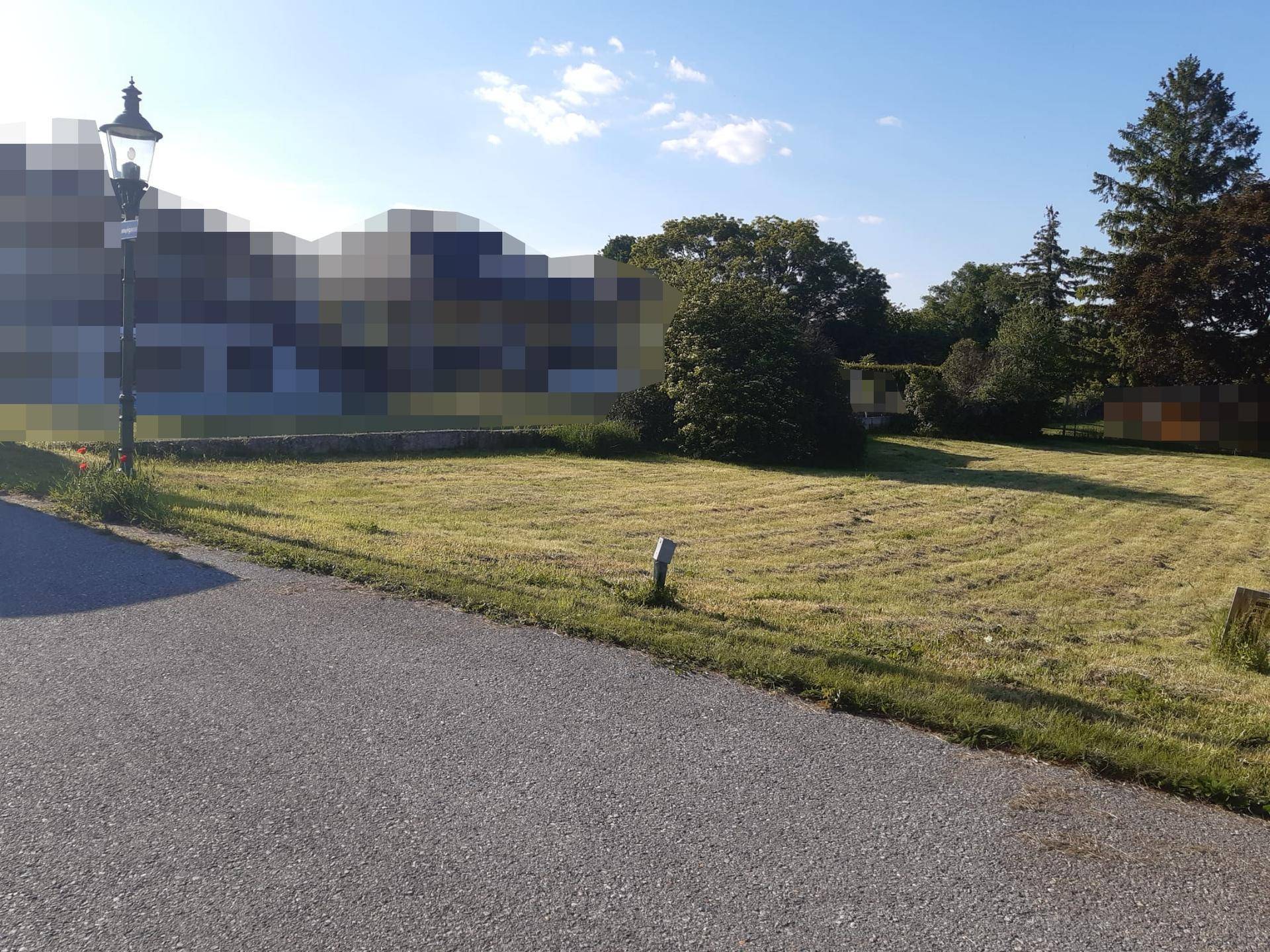 Grundstück mit Rasenfläche, angrenzender Straße und einer klassischen Straßenlaterne.