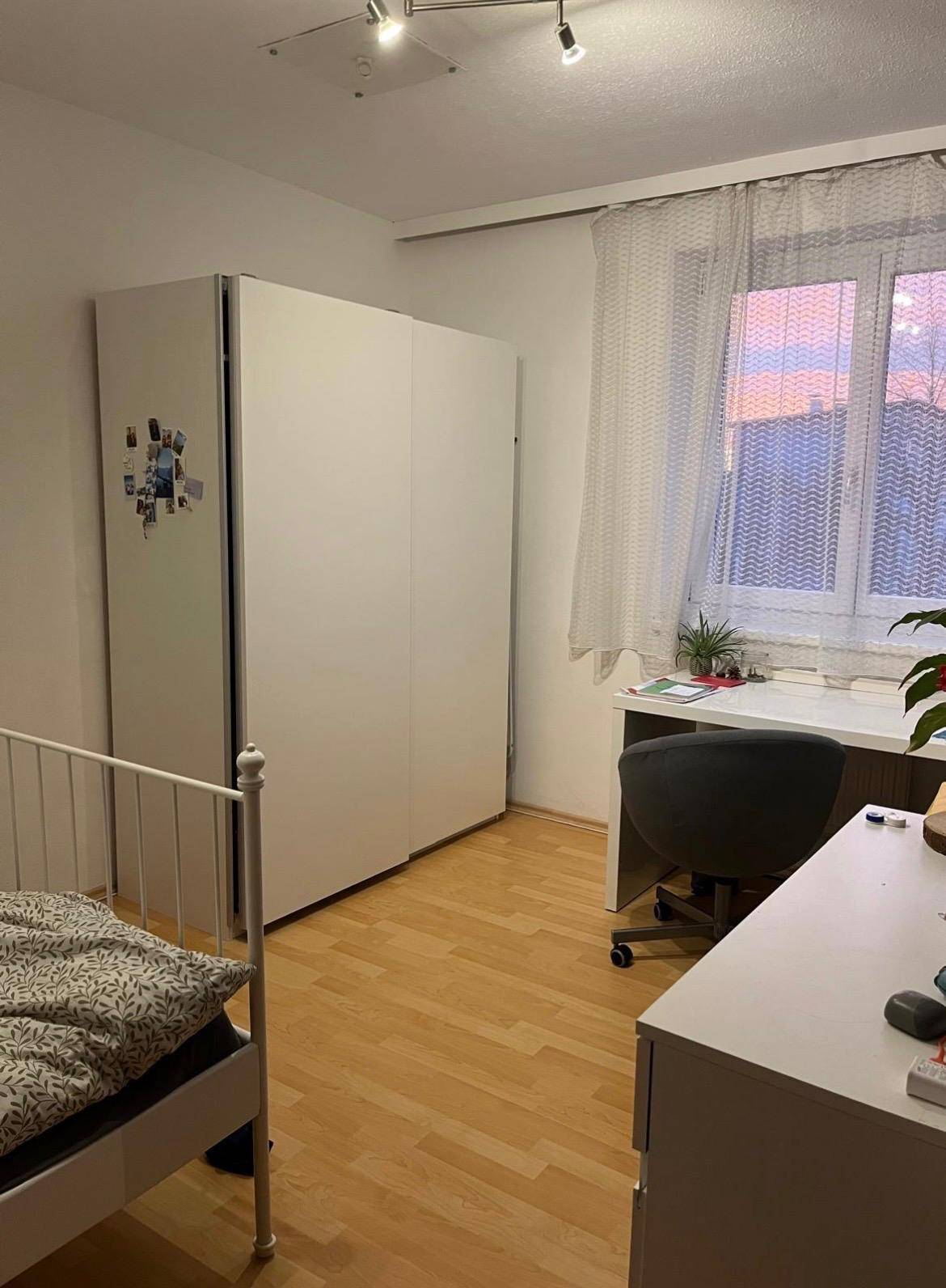 Gemütliches Schlafzimmer mit Einzelbett, weißem Kleiderschrank und Schreibtisch am Fenster.