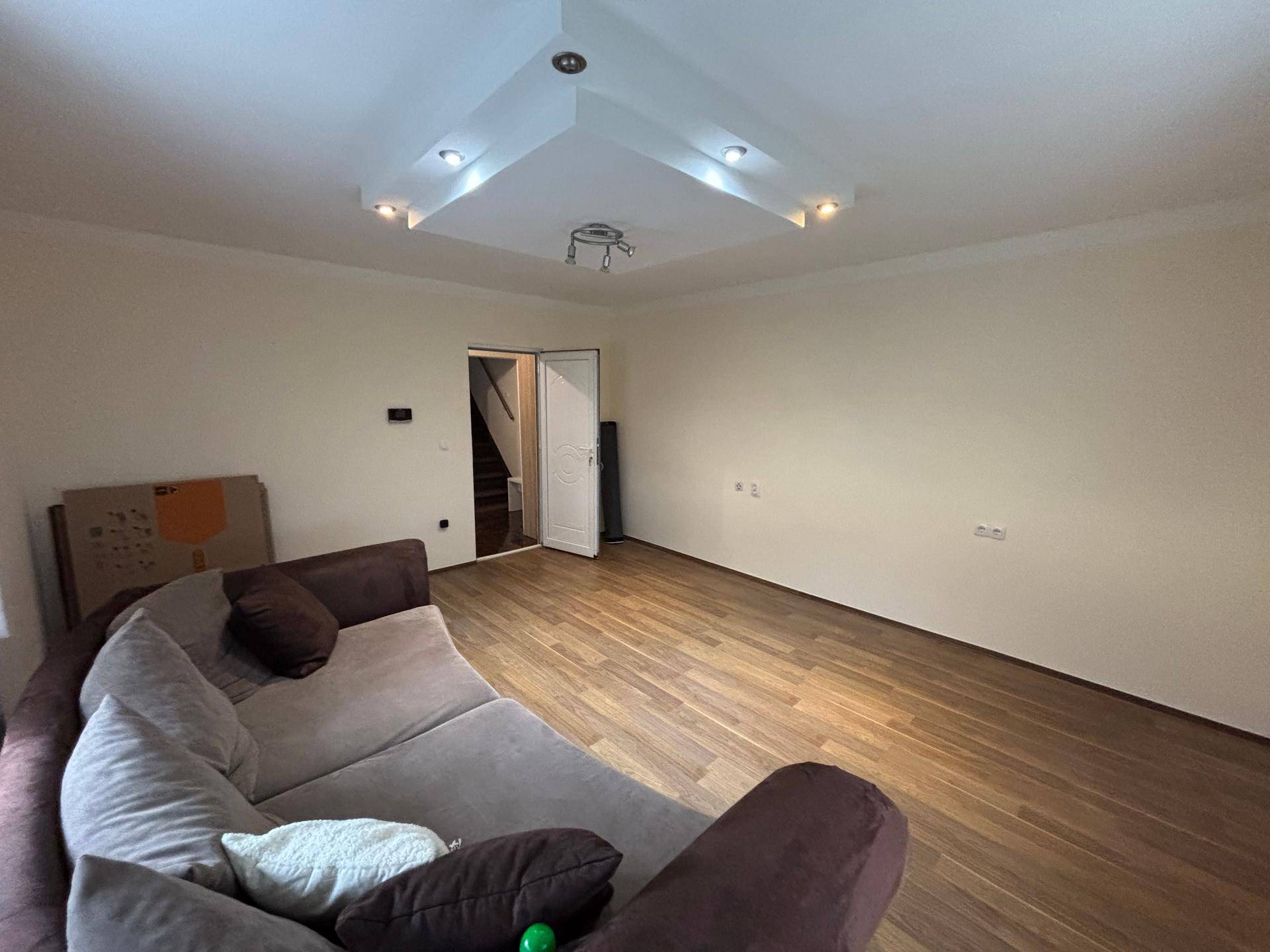 Wohnzimmer mit Laminatboden und Zugang zu einem weiteren Raum, gut beleuchtet.