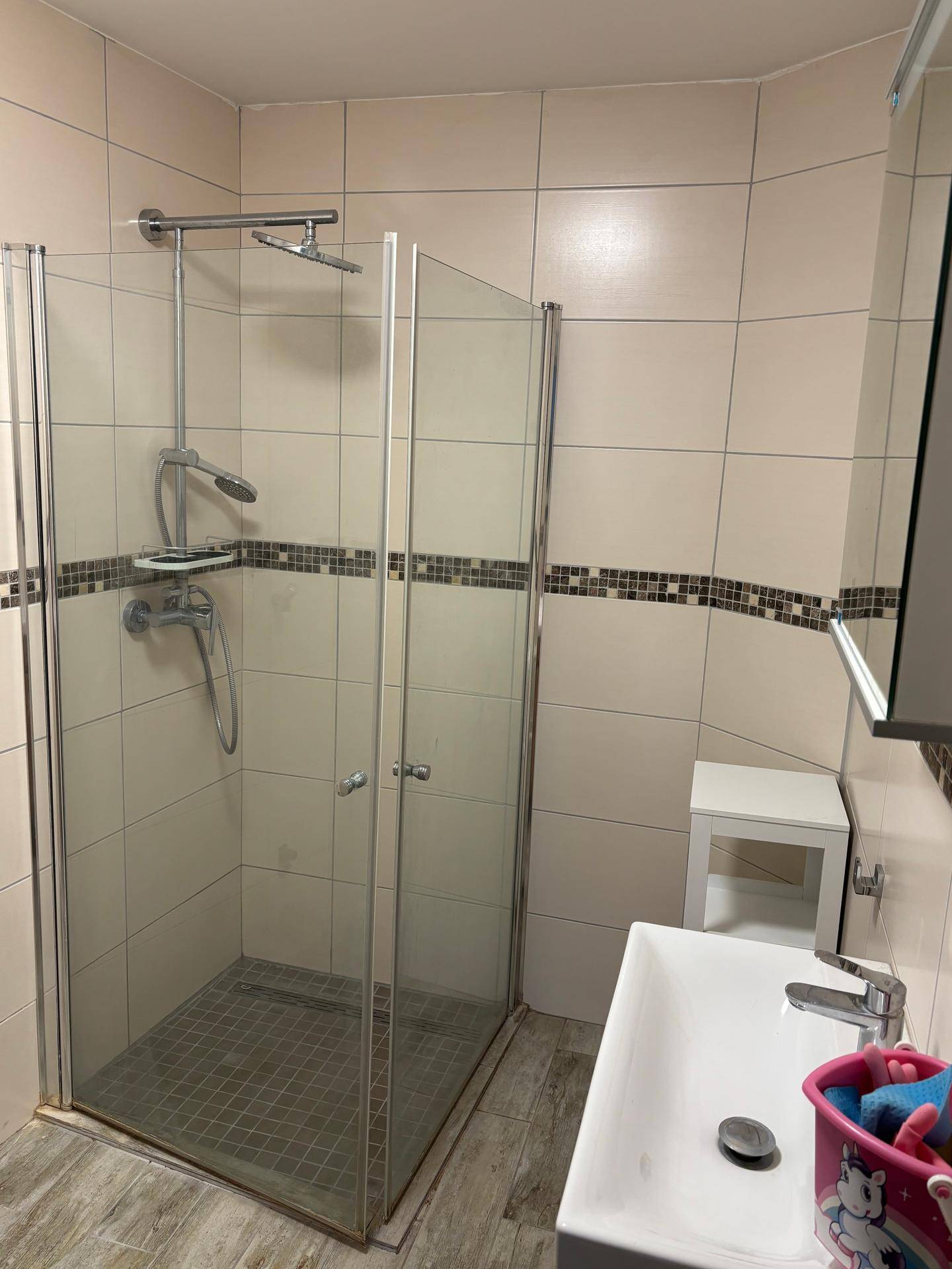 Badezimmer mit Duschkabine, beigefarbenen Fliesen und modernem Waschtisch.
