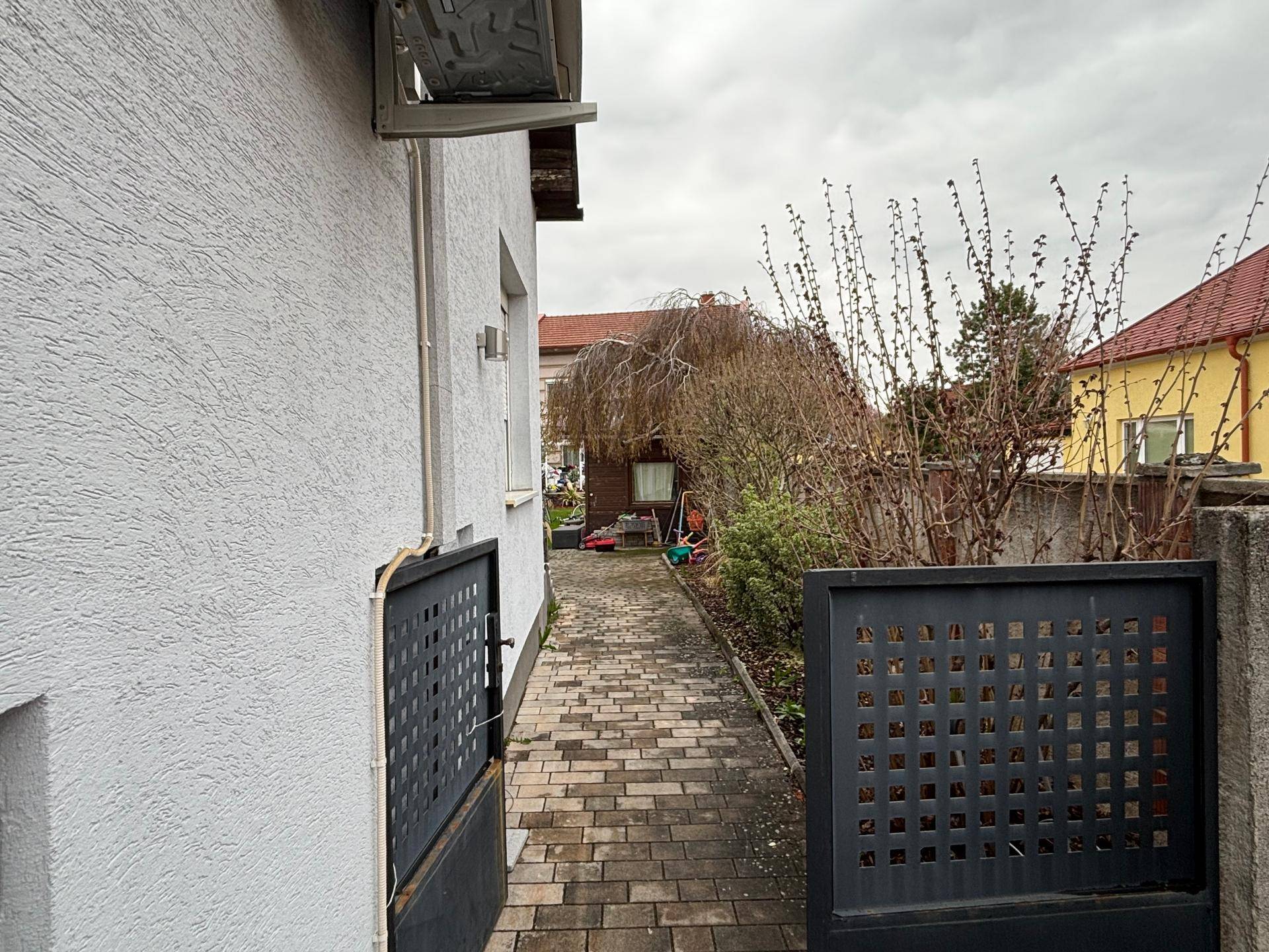 Gepflasterter Seitenweg entlang des Hauses, der zum hinteren Gartenbereich führt.
