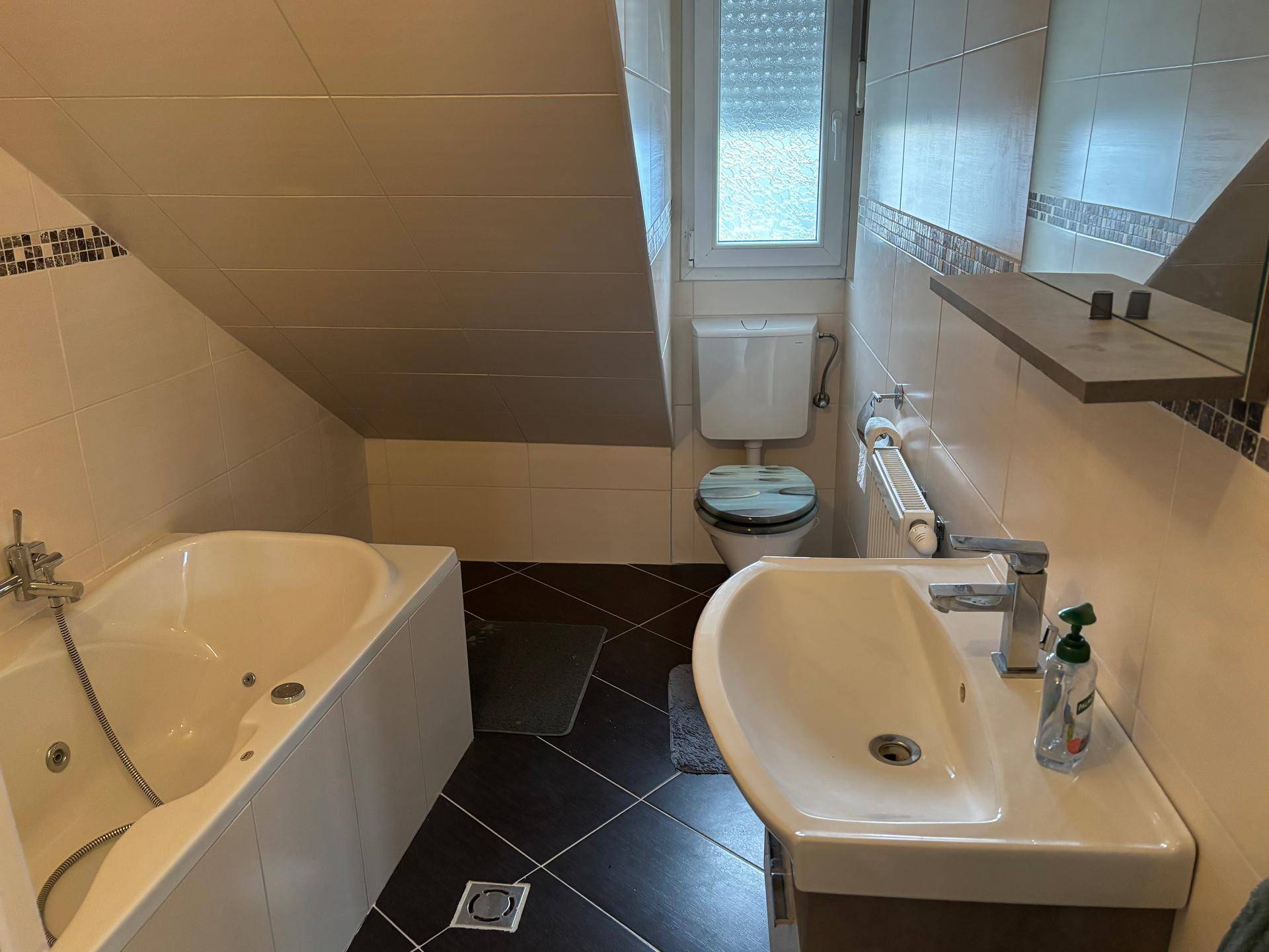 Badezimmer im Dachgeschoss mit Waschtisch, Badewanne und WC, hell gefliest.
