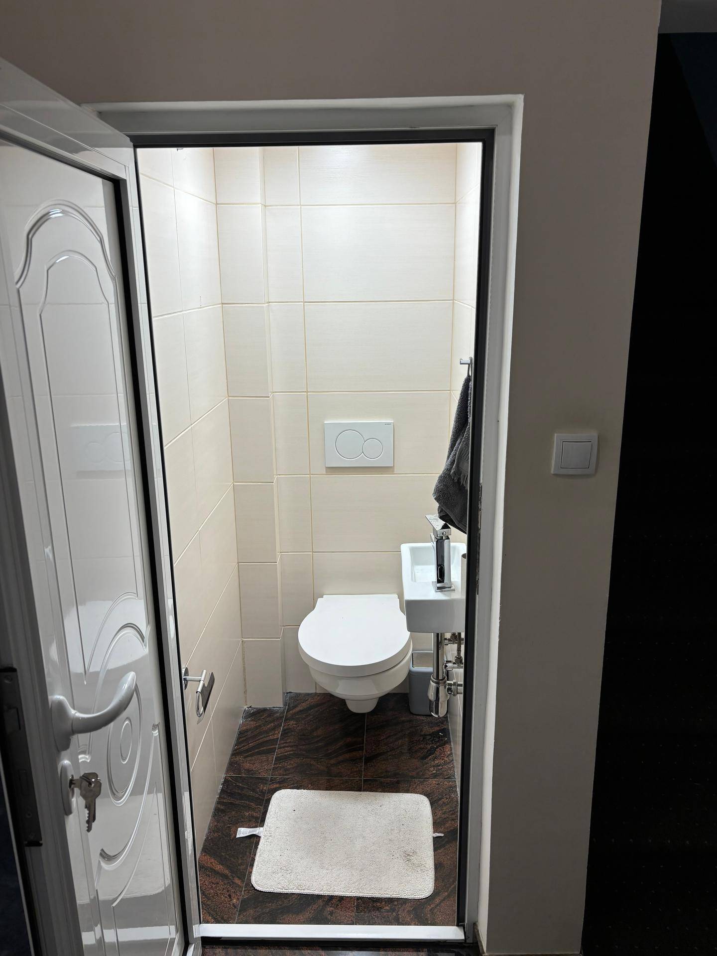 Kleines Gäste-WC mit Wand-WC und Handwaschbecken, hell gefliest.