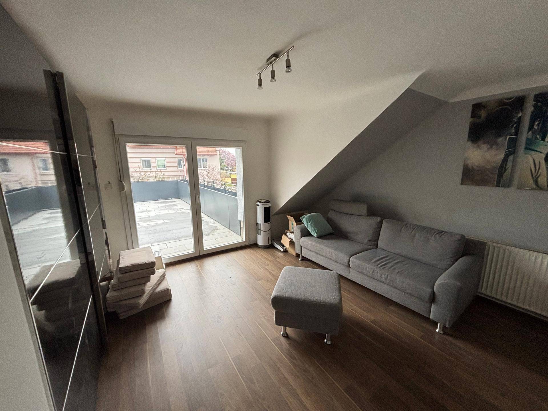 Wohnzimmer im Dachgeschoss mit Zugang zu einer großen Dachterrasse und Laminatboden.