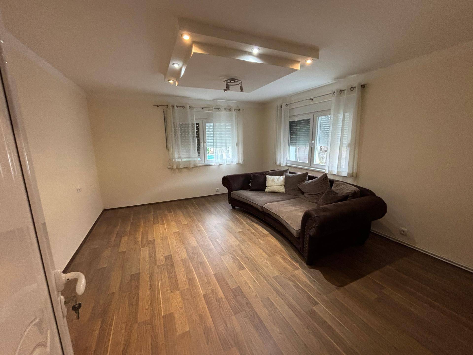 Geräumiges Wohnzimmer mit Laminatboden und einer großen, geschwungenen Couch.