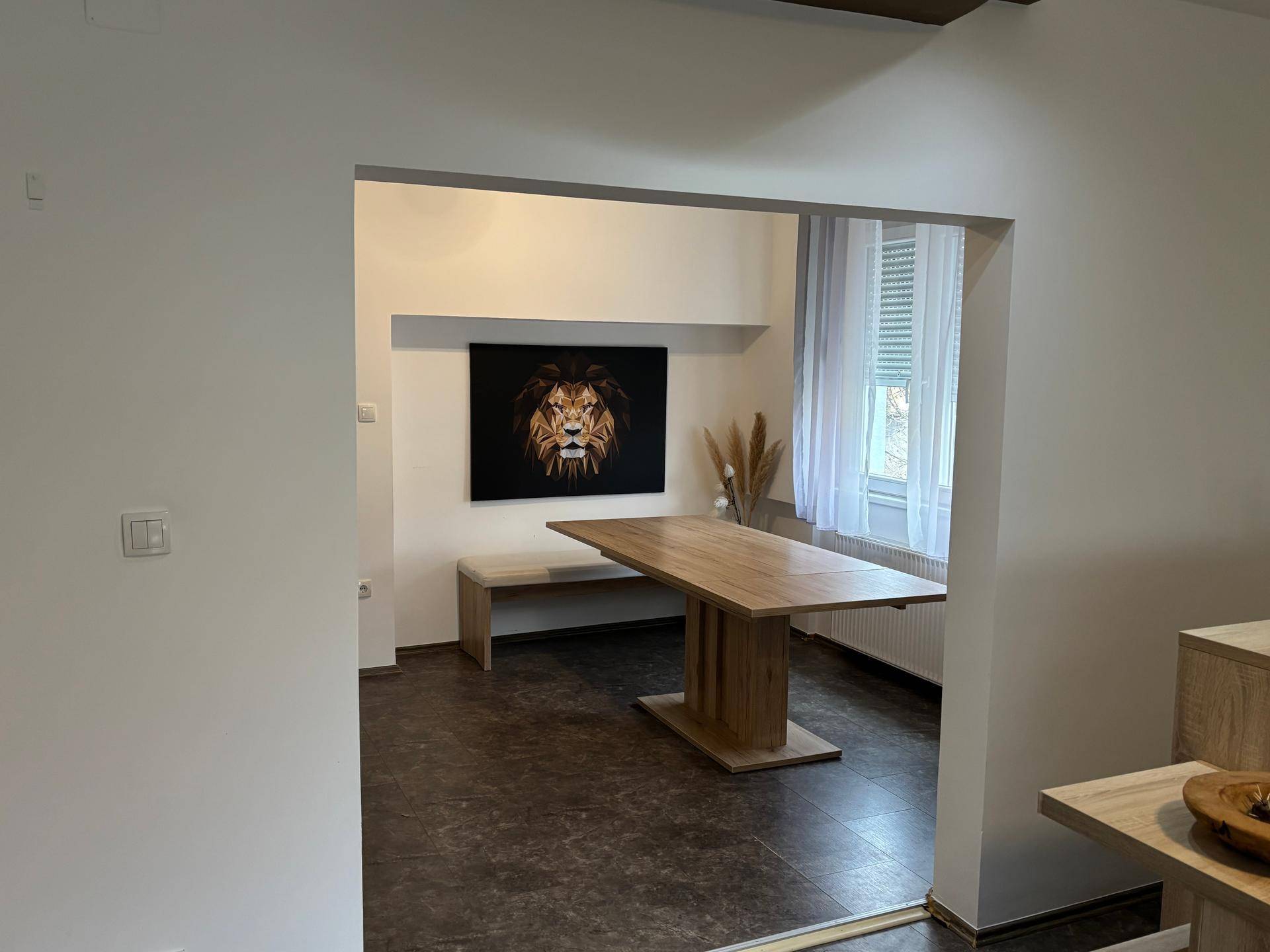 Essbereich mit großem Holztisch und Bank, verbunden mit der Küche durch einen offenen Durchgang.