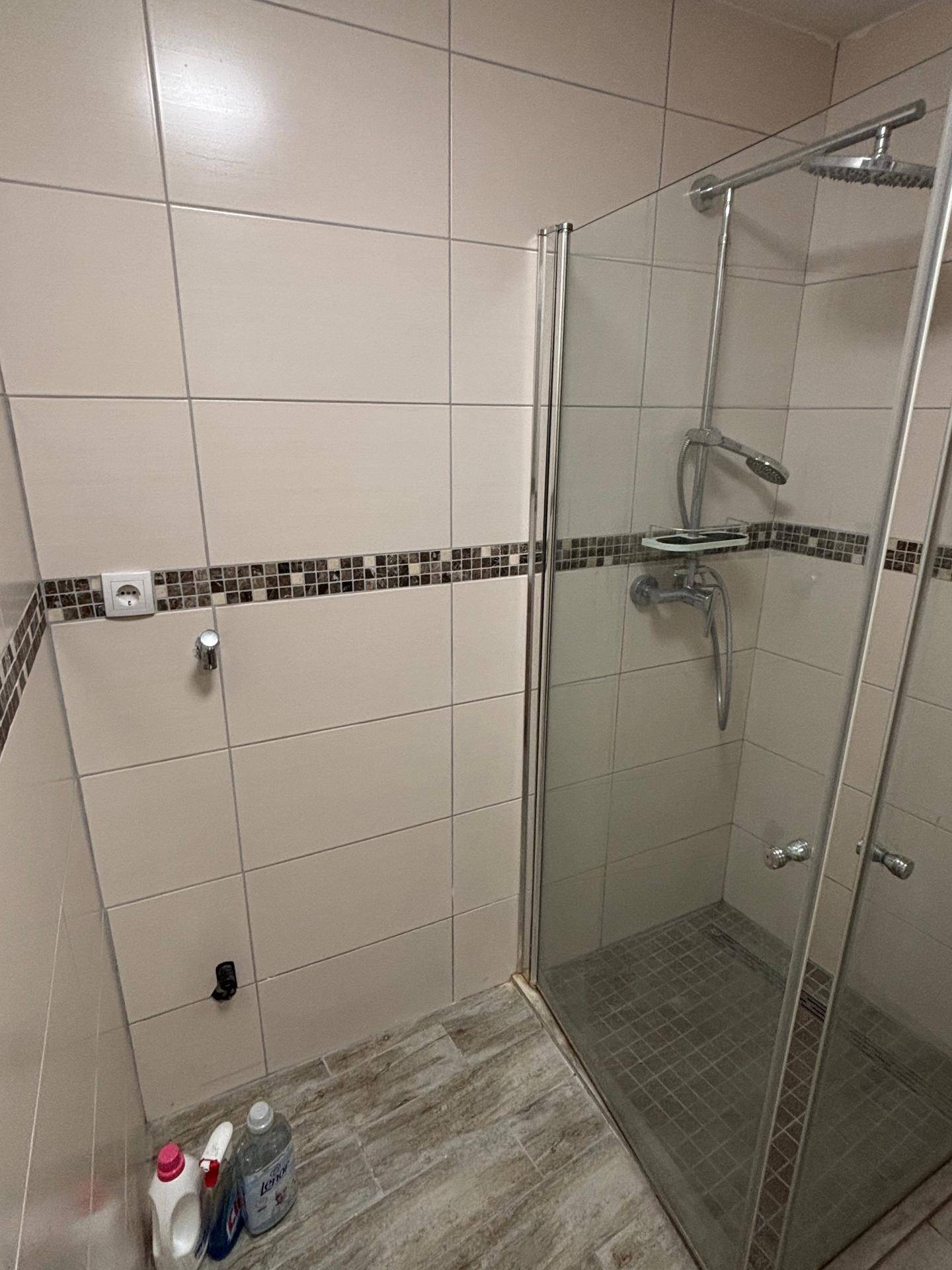 Duschbereich im Badezimmer mit beigefarbenen Fliesen und Glasabtrennung.