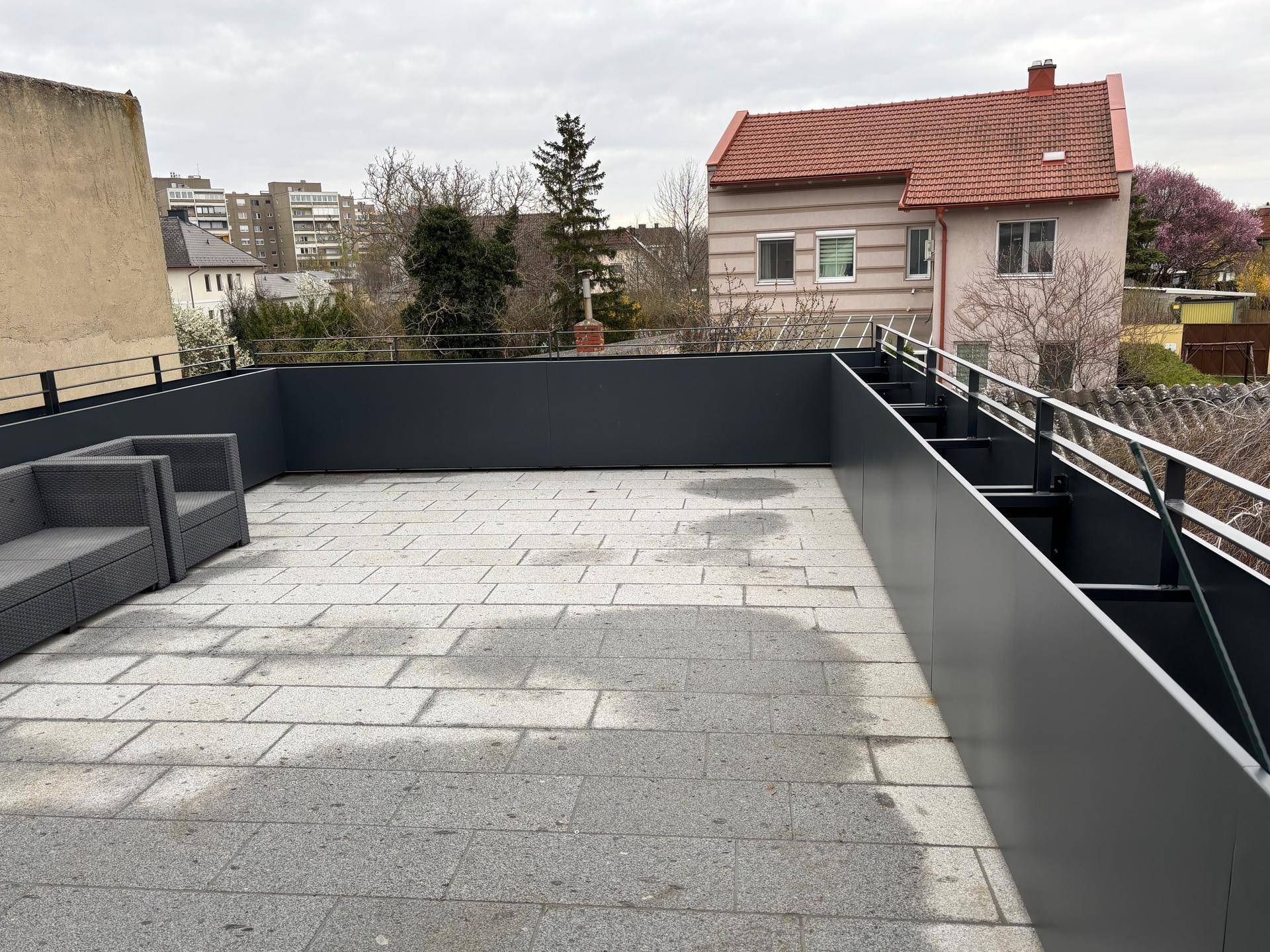 Weitläufige Dachterrasse mit grauen Fliesen und Blick auf die umliegenden Häuser.