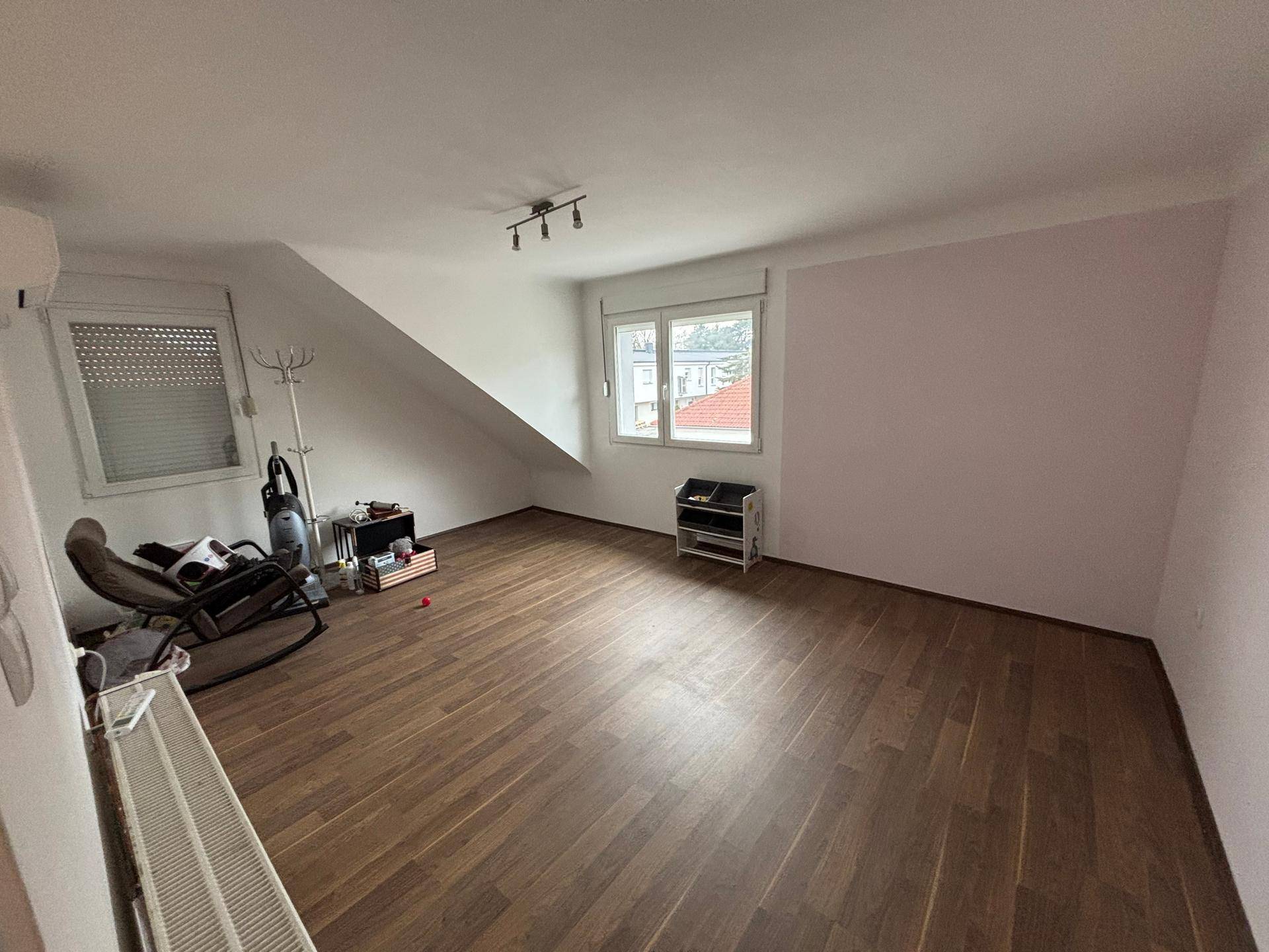 Helles Schlafzimmer im Dachgeschoss mit Schrägdach, Laminatboden und Fenster.