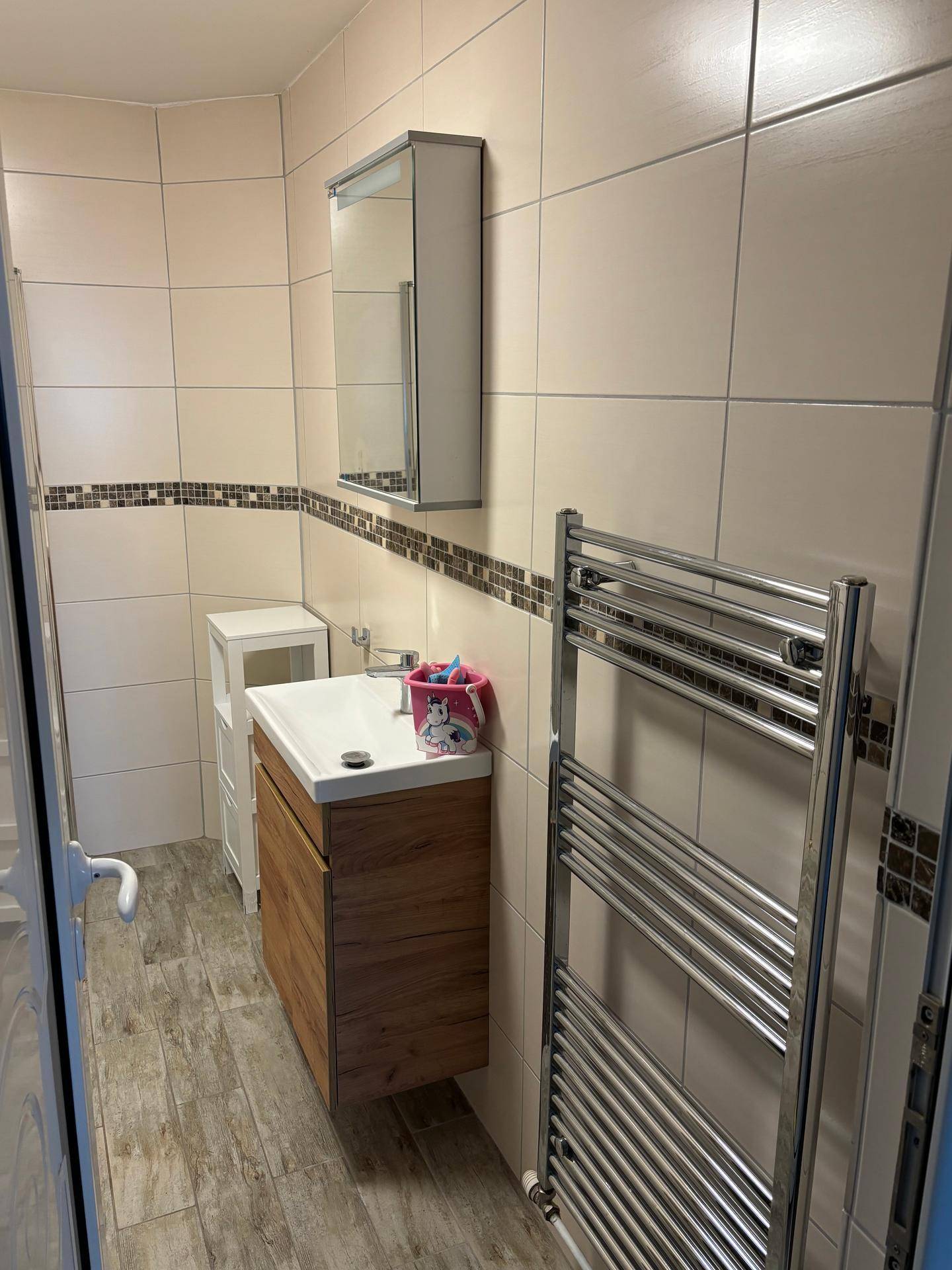 Modernes Badezimmer mit beigefarbenen Fliesen, Waschtisch und beheiztem Handtuchhalter.