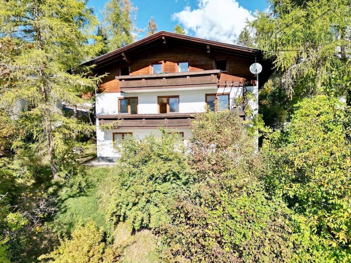 Rückansicht des Hauses mit mehreren Holzbalkonen, umgeben von üppiger Vegetation und Bäumen.