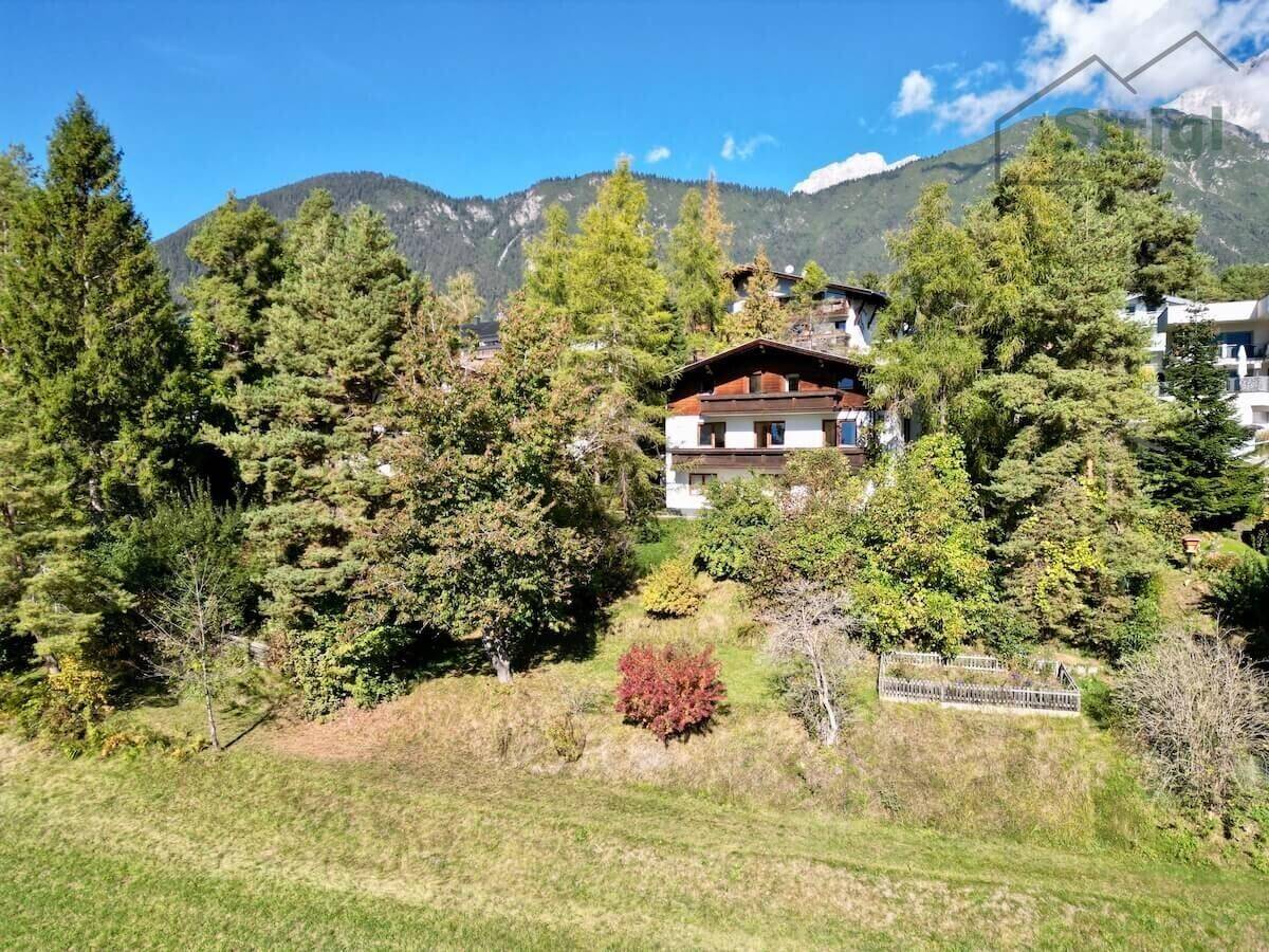 Charmantes Haus umgeben von hohen Bäumen mit einem beeindruckenden Bergpanorama im Hintergrund.